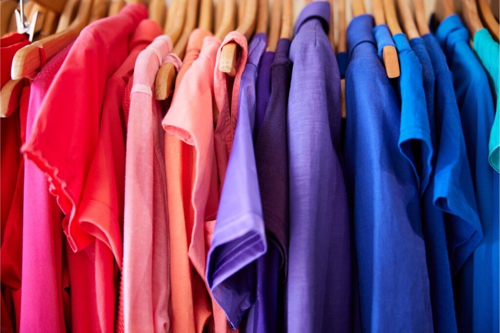 Personal color analysis: a clothes rack with tightly packed women's shirts of multiple colours (pinks, purples and blues) on wooden hangers.
